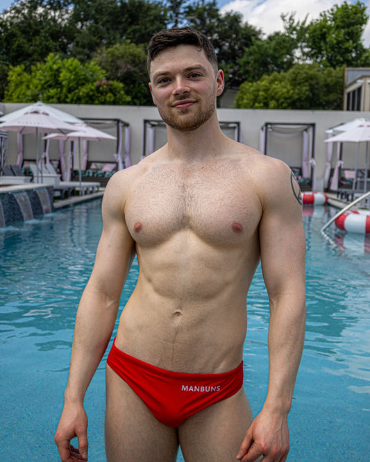 man standing at the pool shirtless wearing a red swim brief with the brand logo on the right hip