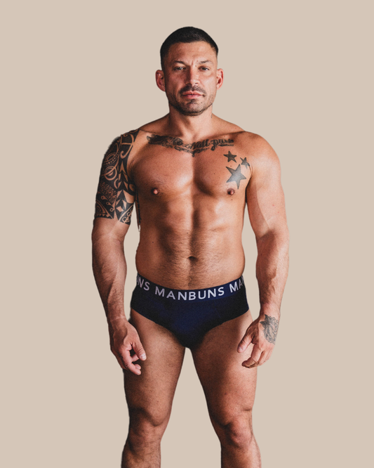 Man wearing black underwear with 'MANBUNS' branding against a beige background